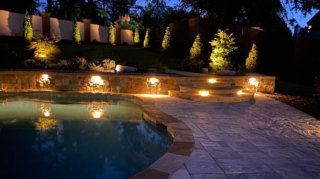 A swimming pool is lit up at night in a backyard.