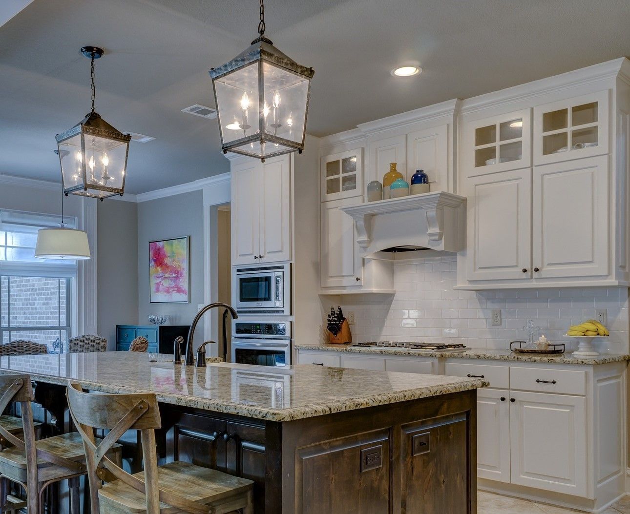Kitchen with white cabinets, granite countertops, island with wooden base, and hanging lanterns.