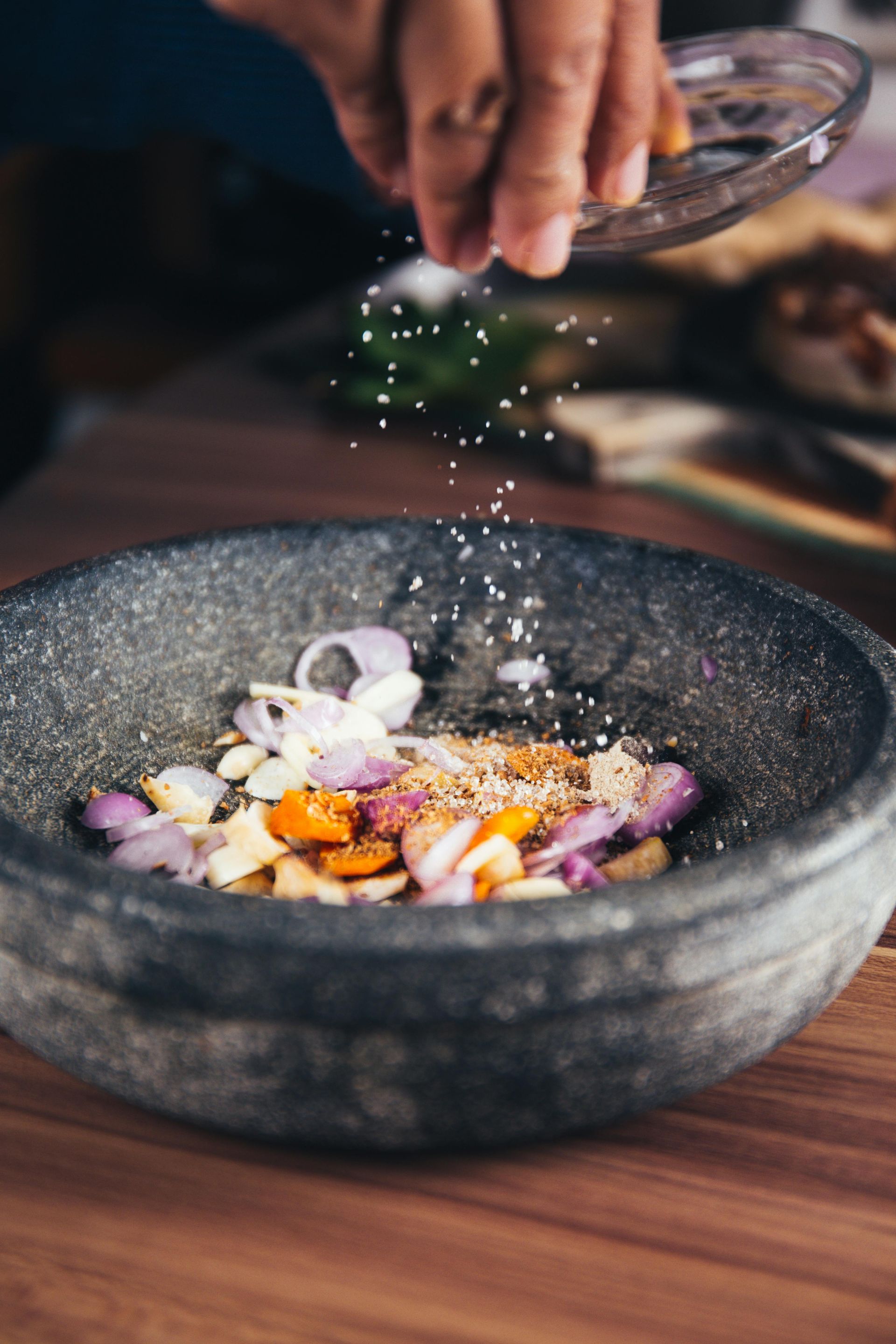 A person is sprinkling salt into a bowl of vegetables.