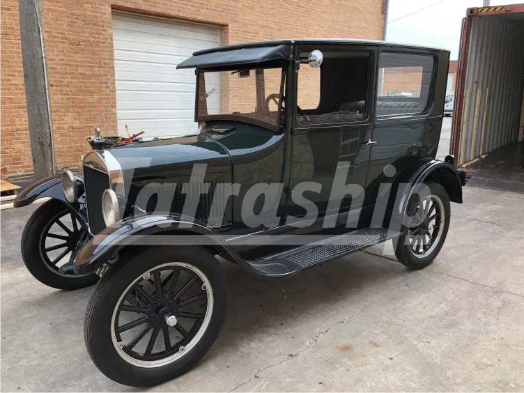 An old black car is parked in front of a garage with the word trashing on it