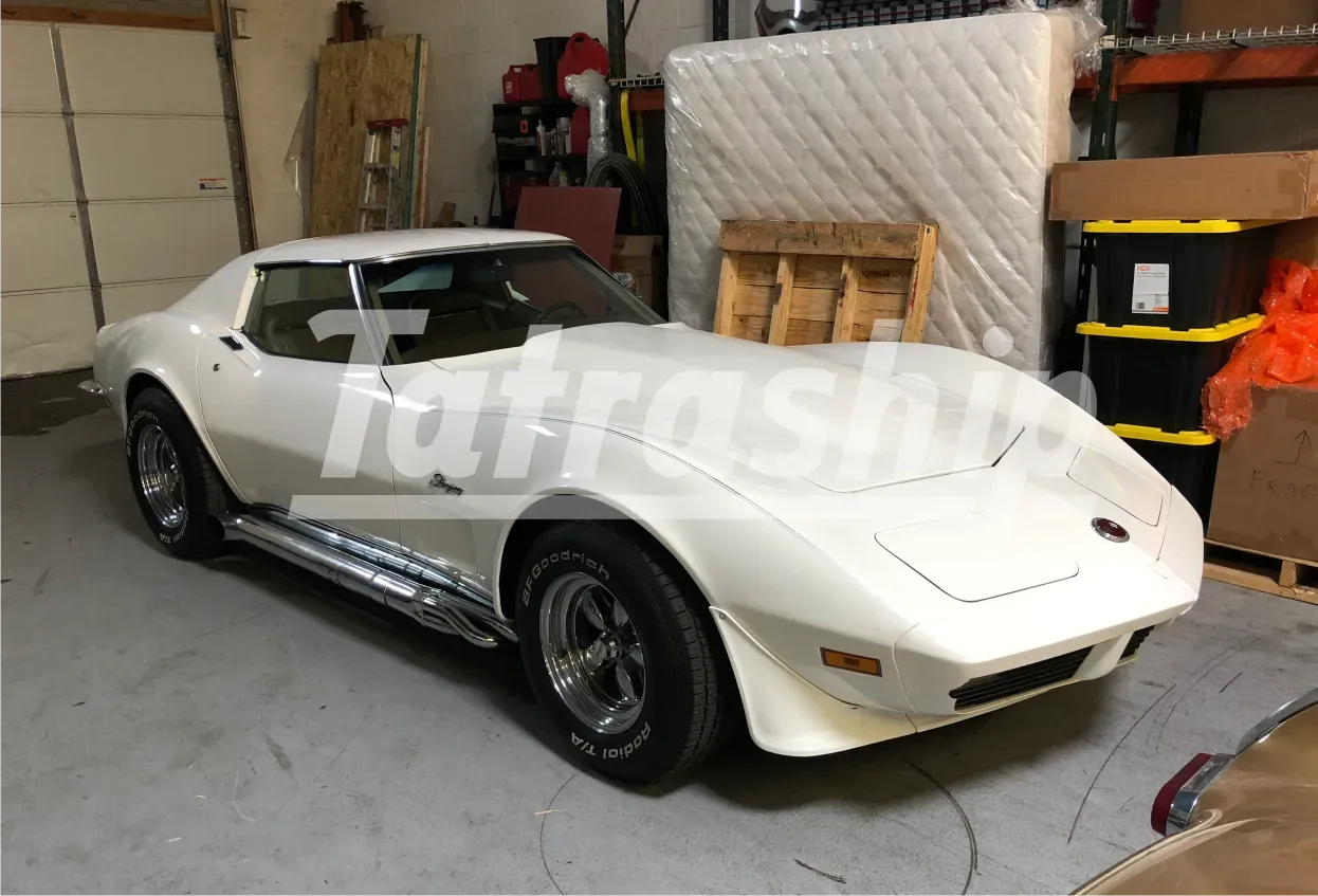 A white corvette is parked in a garage next to a mattress