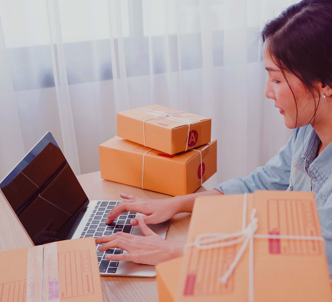 A woman is typing on a laptop next to a stack of boxes.