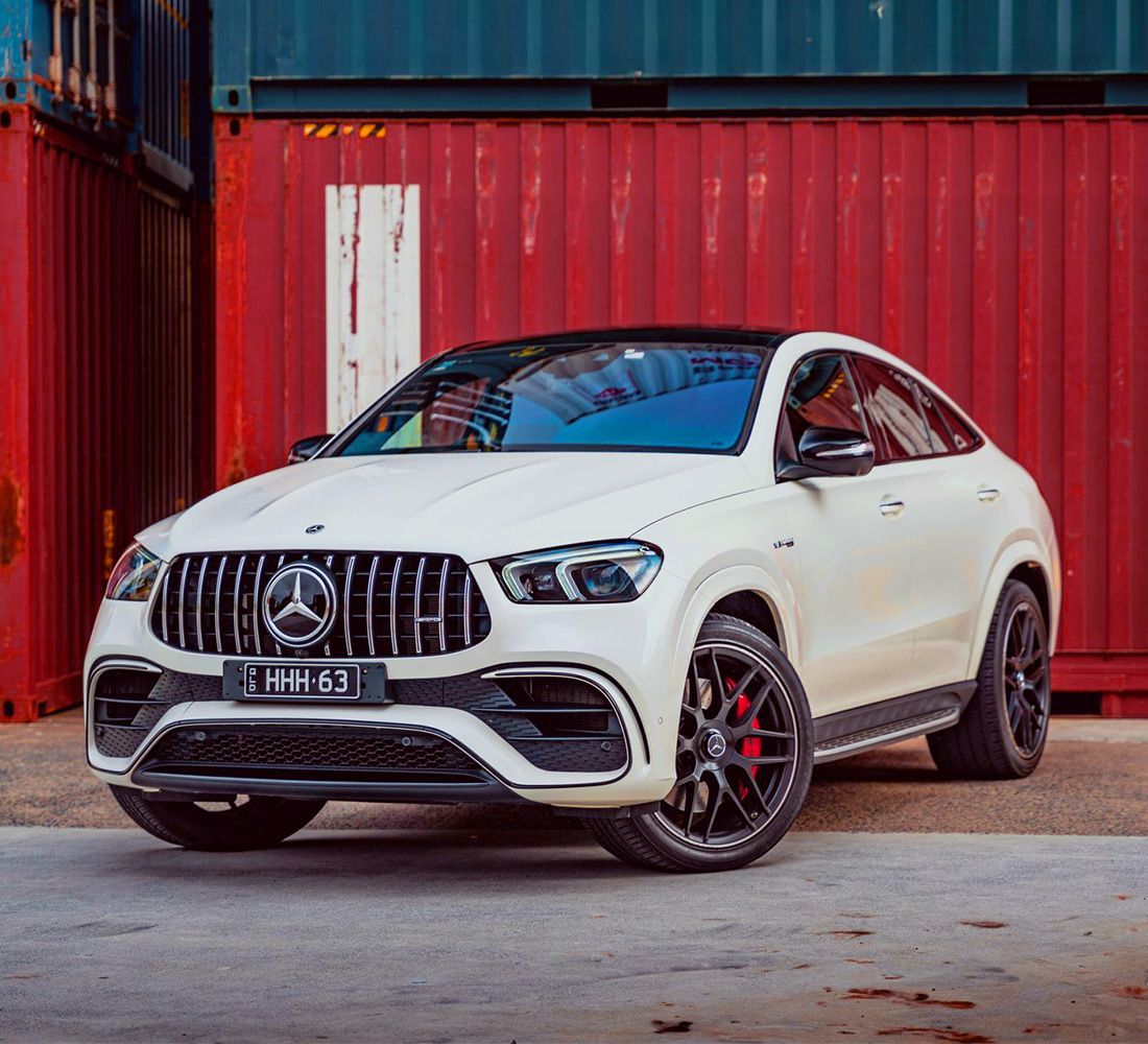 A white mercedes benz gle 63 amg coupe is parked in front of a red container.