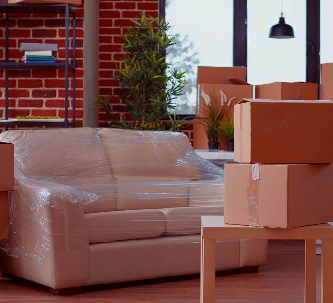 A living room filled with boxes and a couch wrapped in plastic.