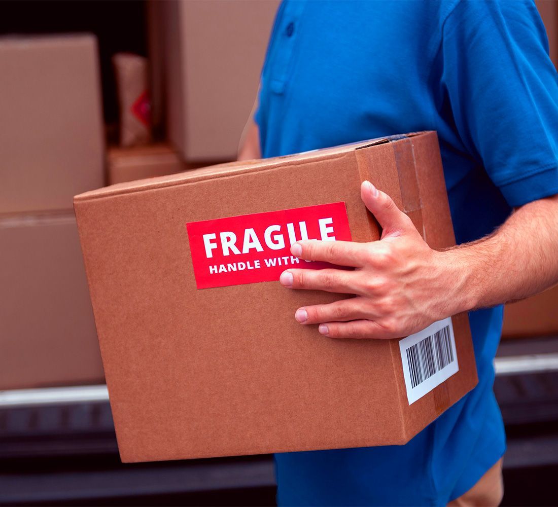 A man in a blue shirt is carrying a cardboard box with a fragile sticker on it