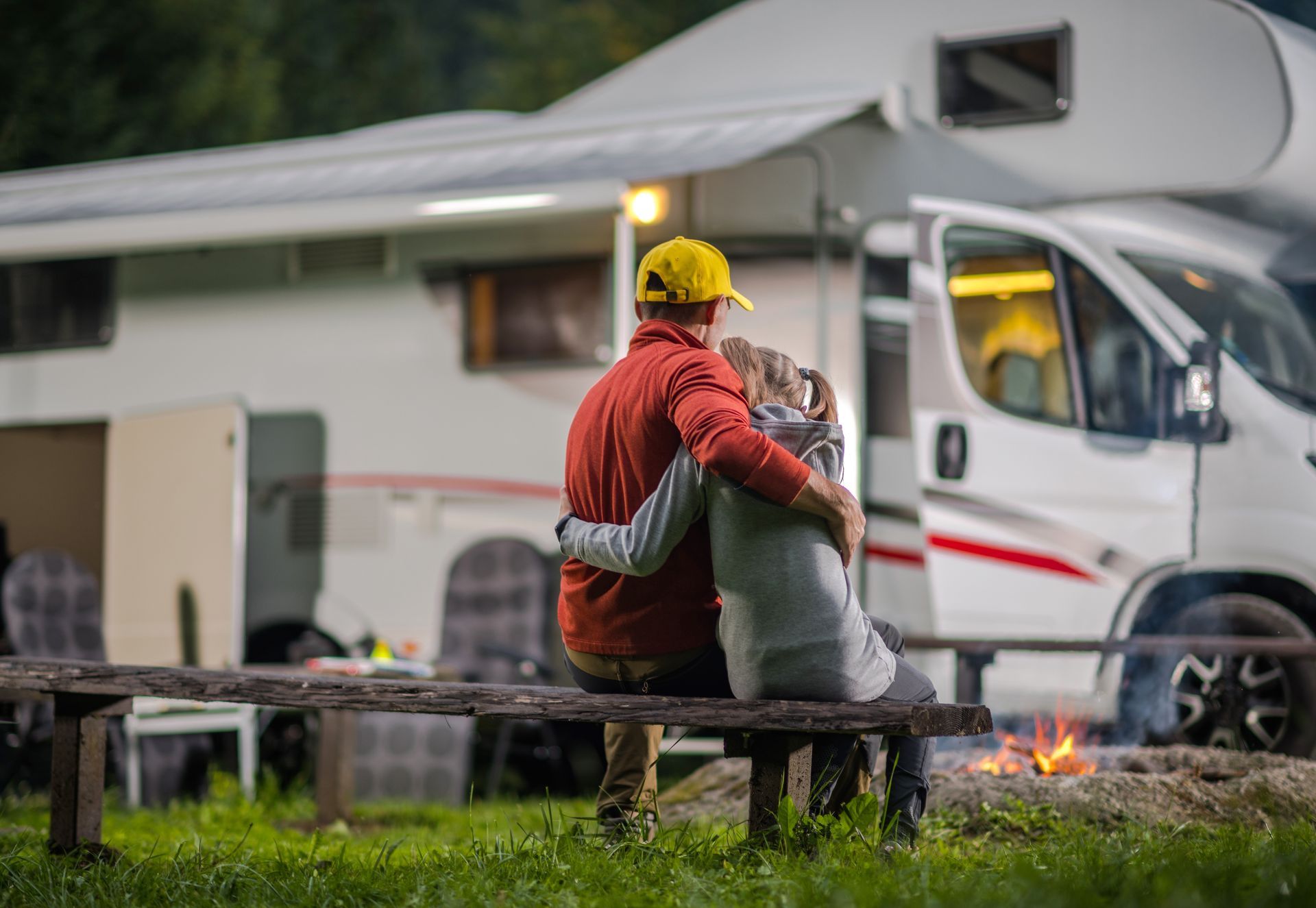 A man and a girl are sitting on a bench in front of an RV