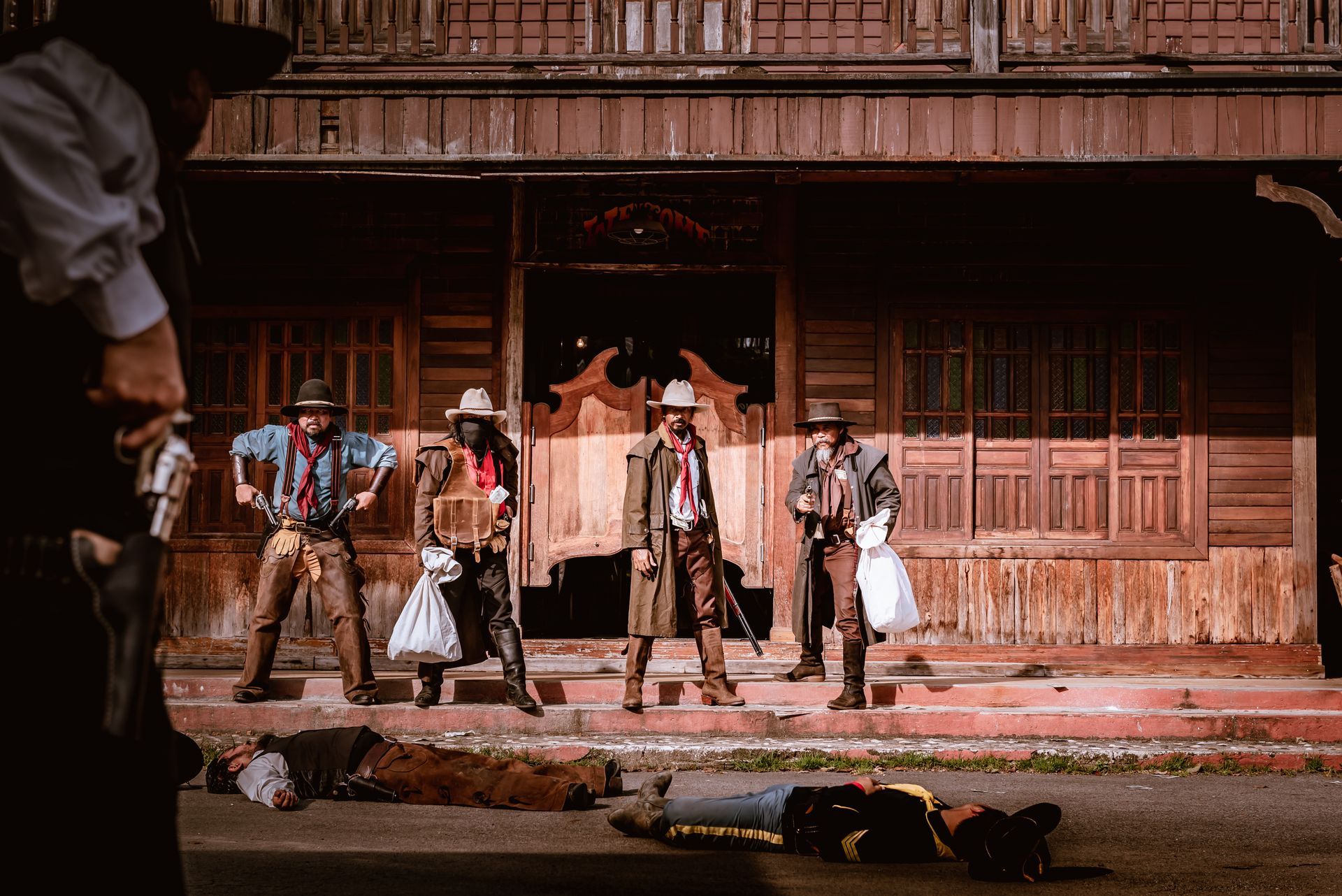 Cowboys stand in front of a saloon after a shootout. Dead bodies are on the ground.