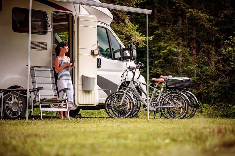 A woman is standing next to a rv with bikes parked in front of it.