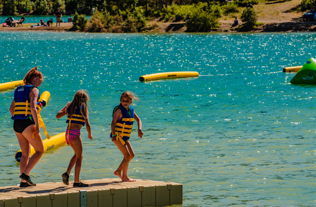 A group of children are standing on a dock in the water.