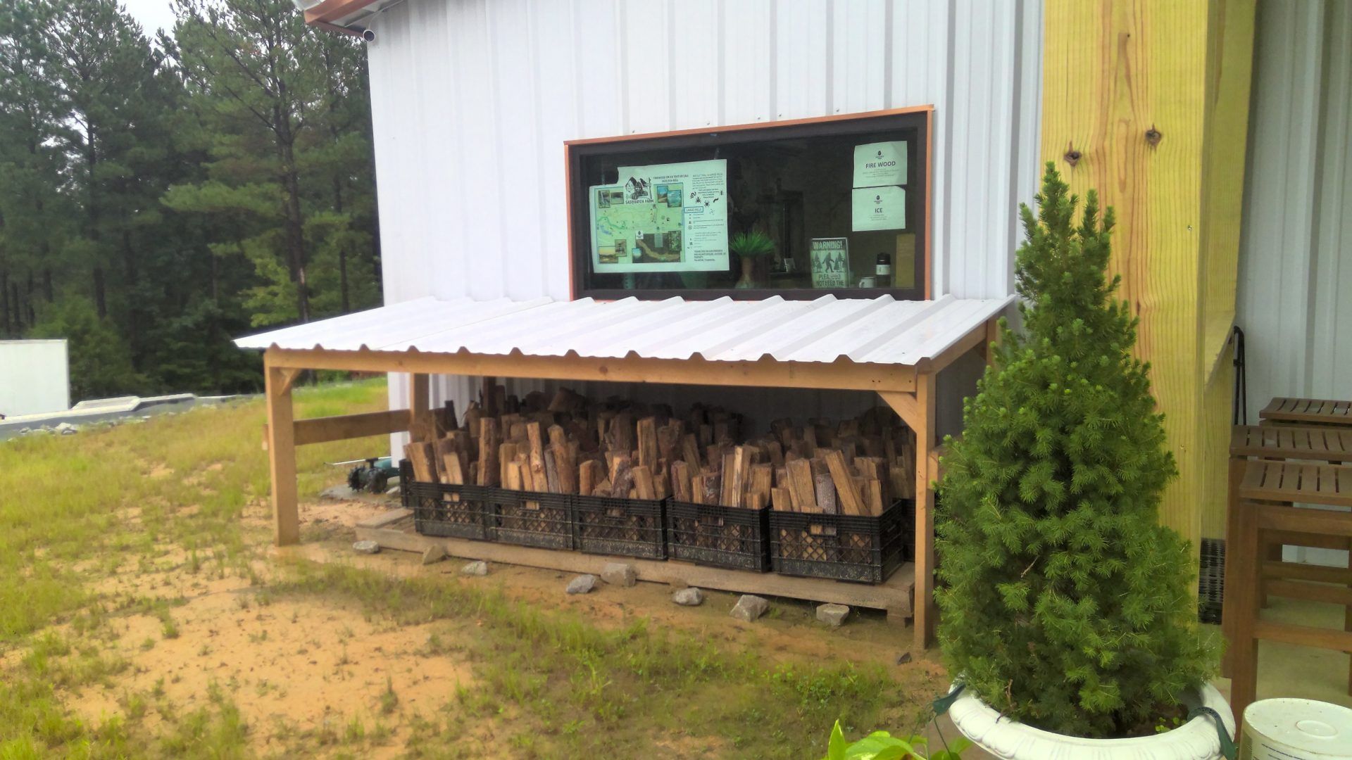 A shed with a roof and a shelf filled with logs in front of it.