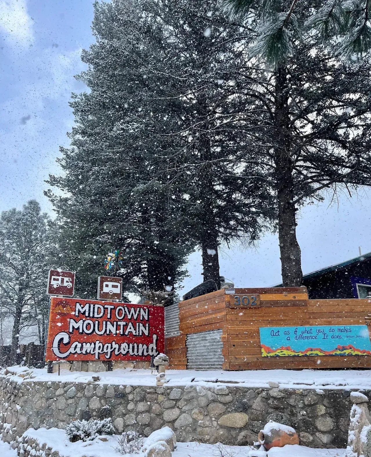 A red sign that says `` midtown mountain campground '' is surrounded by snow covered trees.