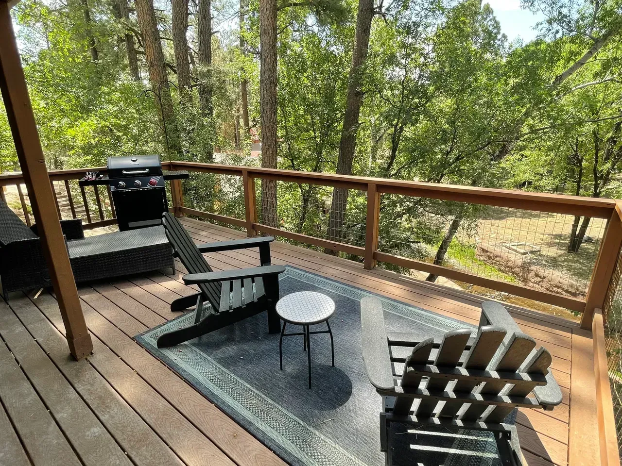 A wooden deck with chairs , a table and a grill.