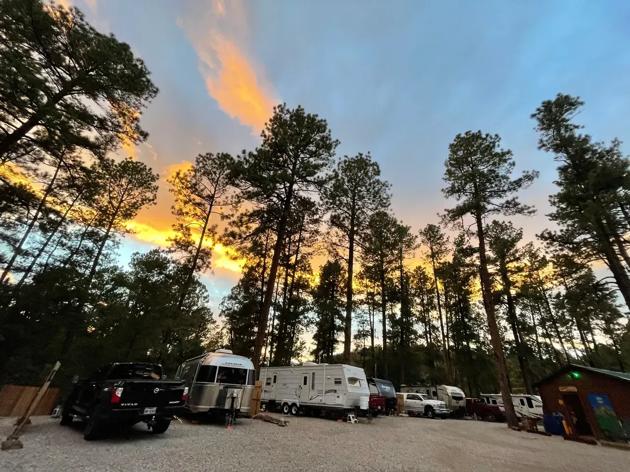 A group of rv 's are parked in a parking lot surrounded by trees at sunset.