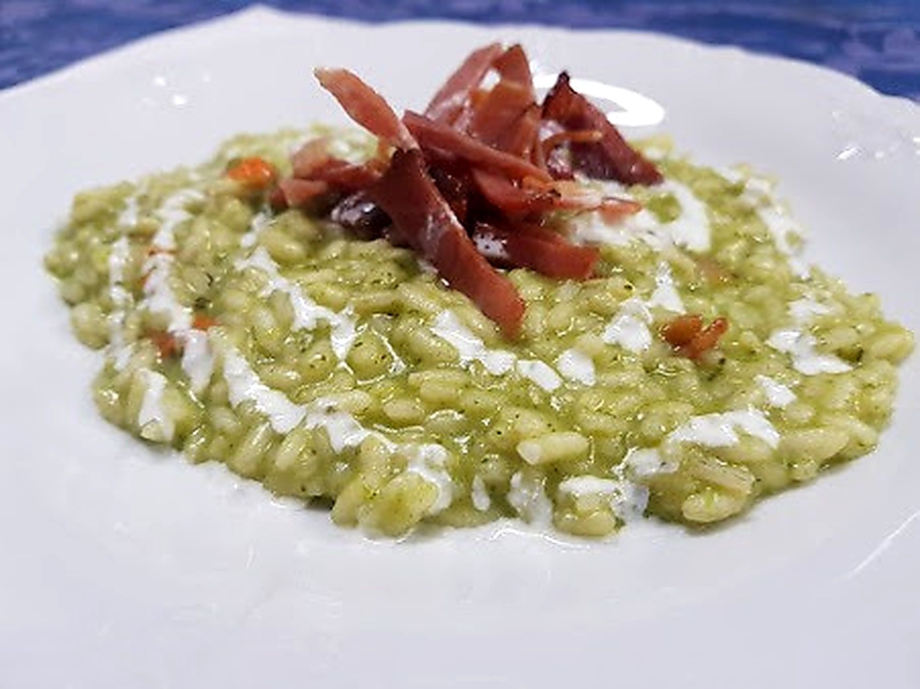 Risotto verde con prosciutto e formaggio bianco cremoso su un piatto bianco.