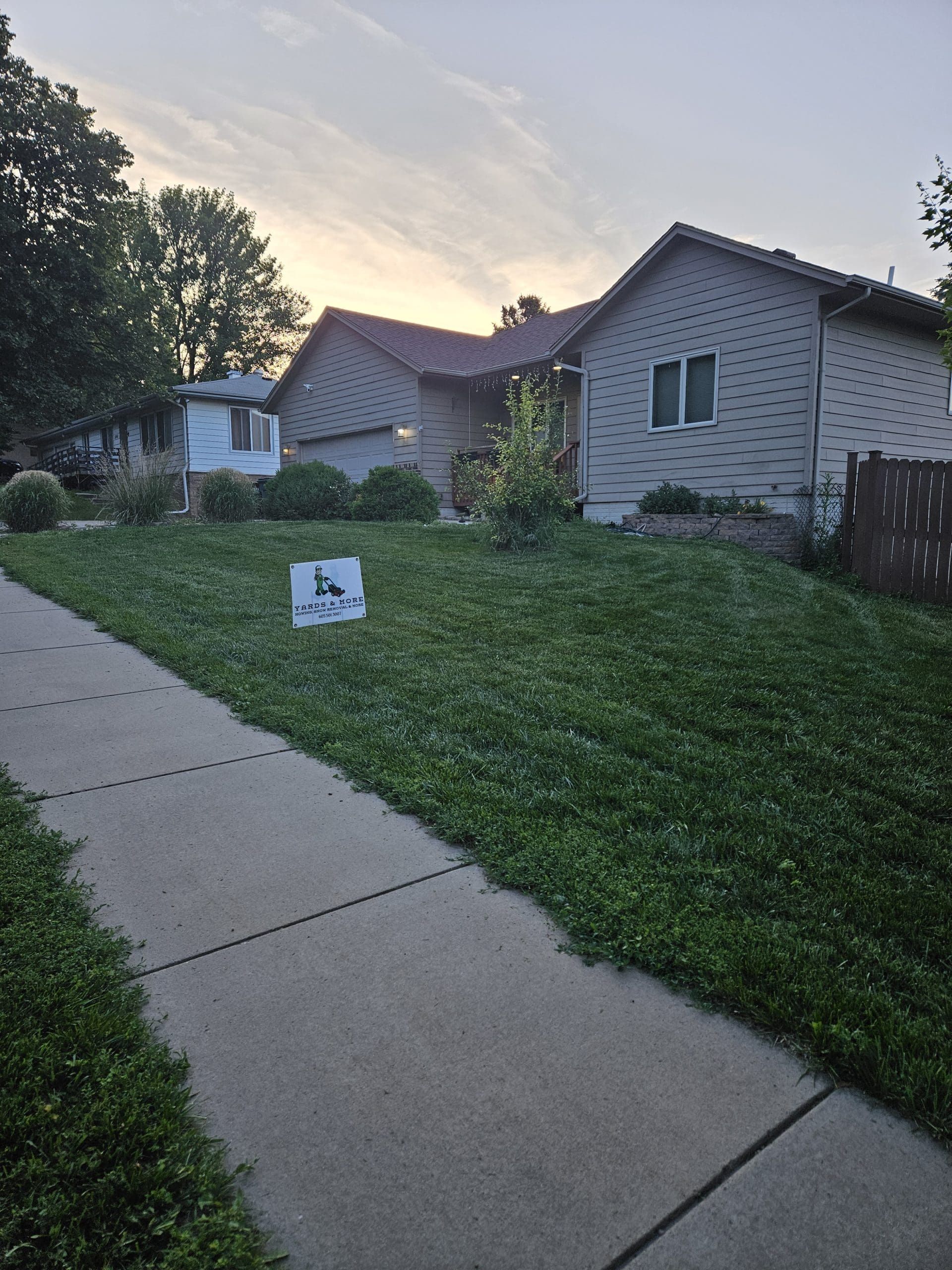 House with light blue siding and reddish-brown roof, green lawn with sidewalk in front.