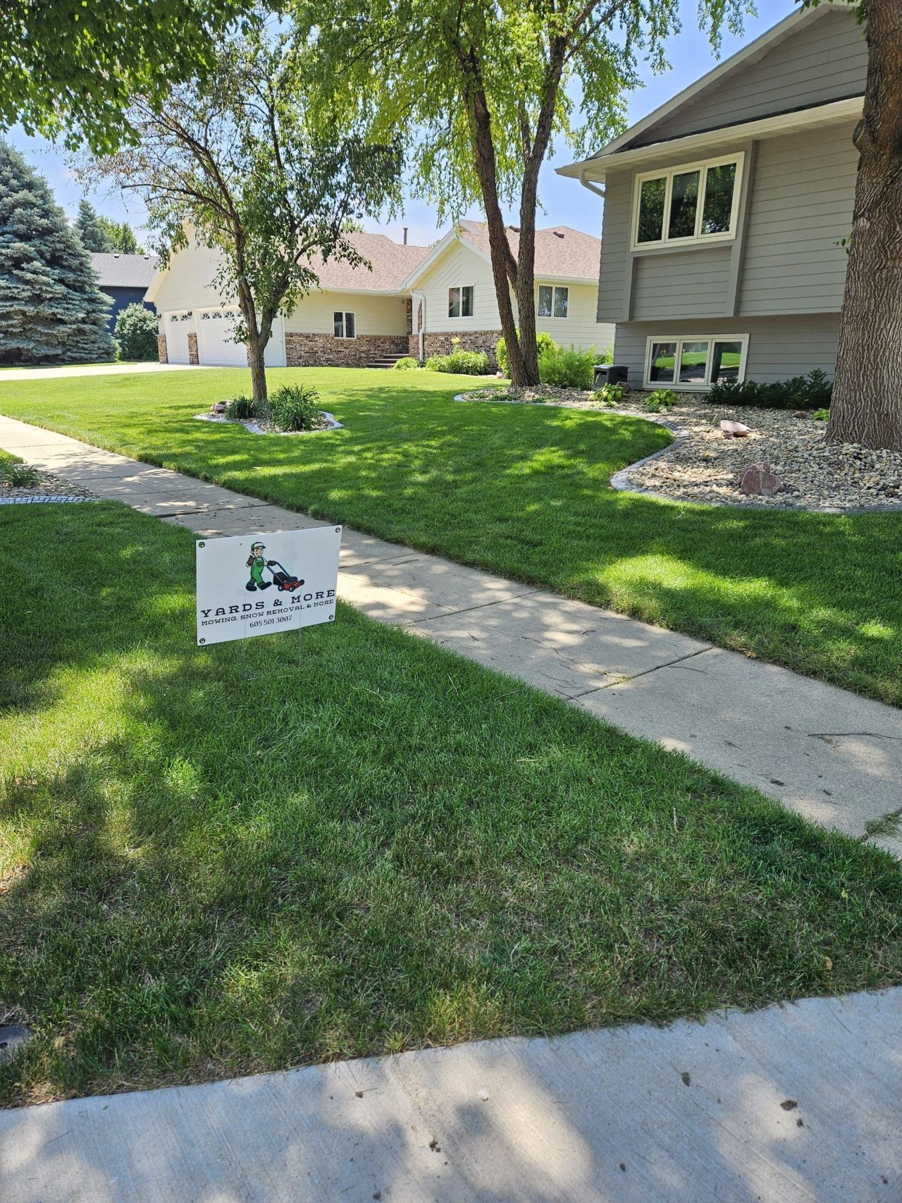 Green lawn with sidewalk, houses in background, and a sign on the lawn.