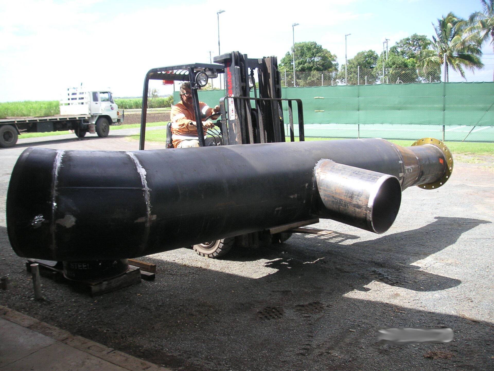 A Man Is Driving A Forklift Carrying A Large Black Pipe — Origin Group in Paget, QLD