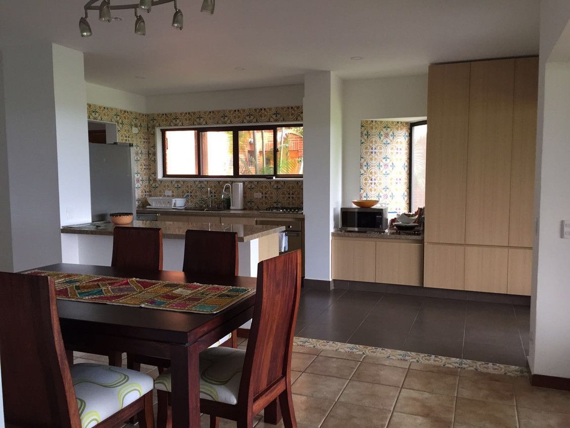 A dining room with a table and chairs and a kitchen in the background.