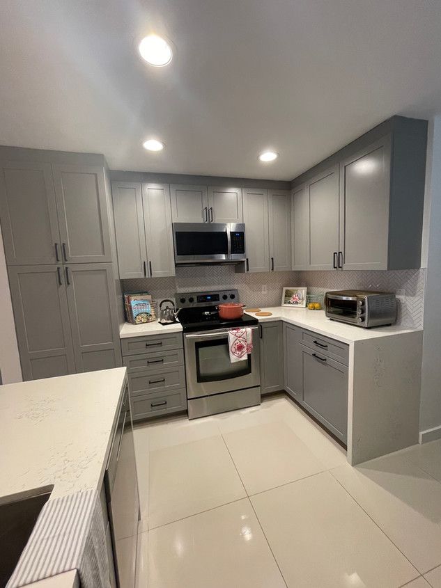 A kitchen with gray cabinets , stainless steel appliances , and white counter tops.