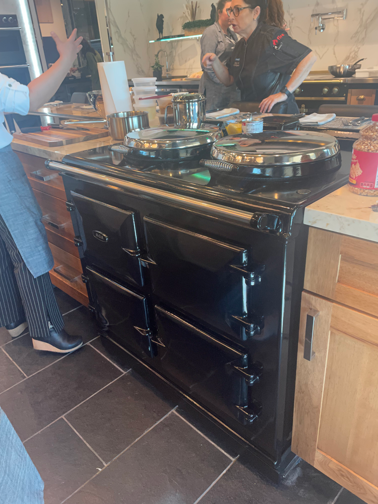 A woman is standing in front of a black stove in a kitchen.