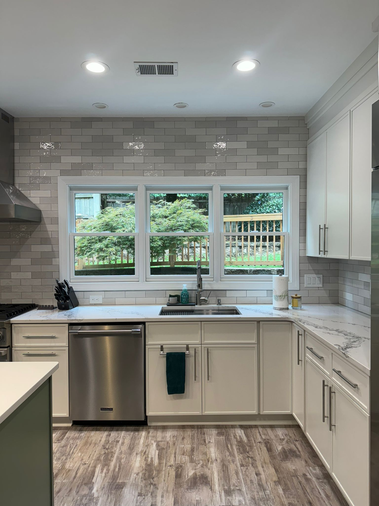 A kitchen with white cabinets , stainless steel appliances , a sink , and a window.