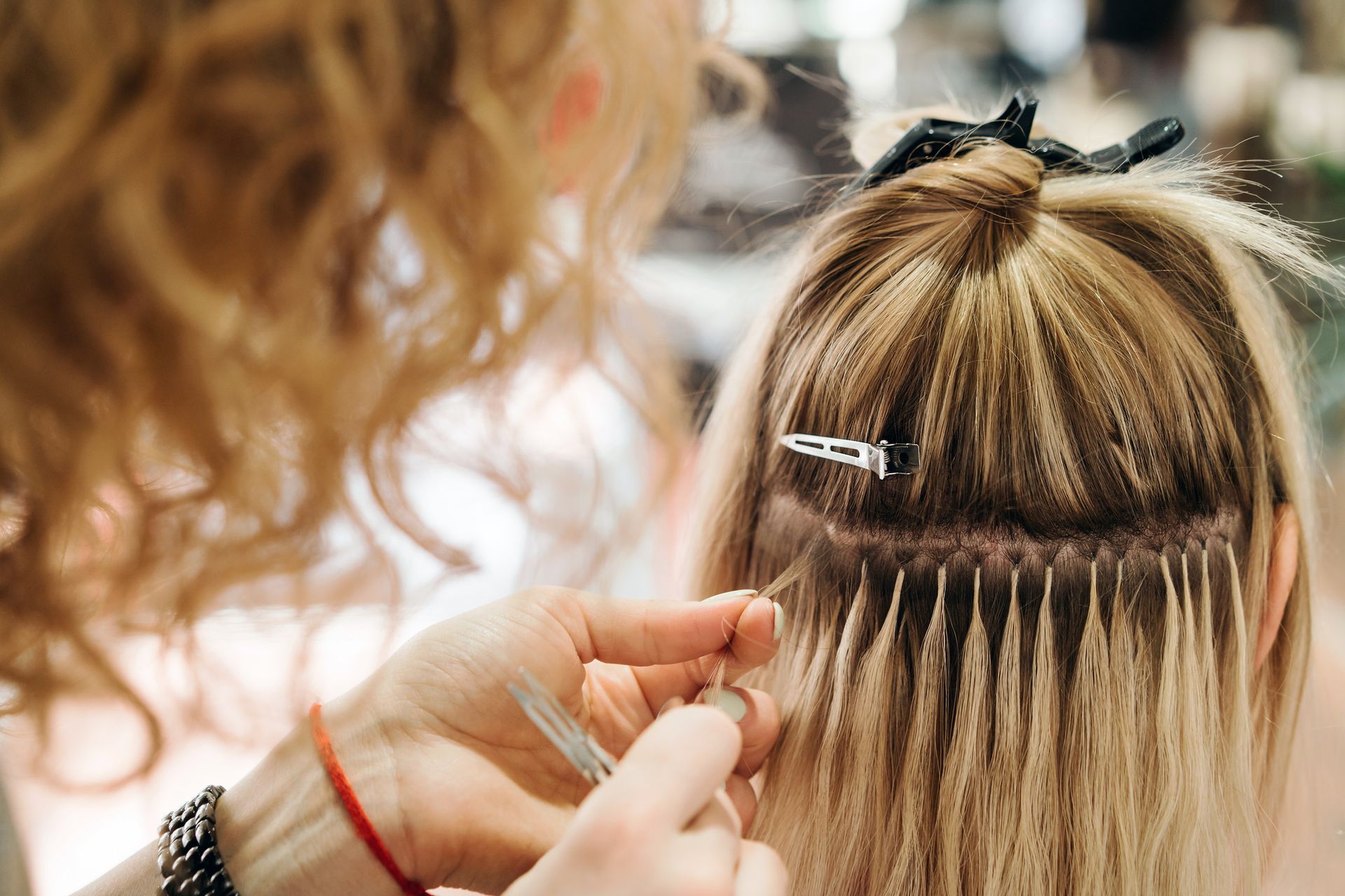 A woman is getting her hair extensions done by a hairdresser