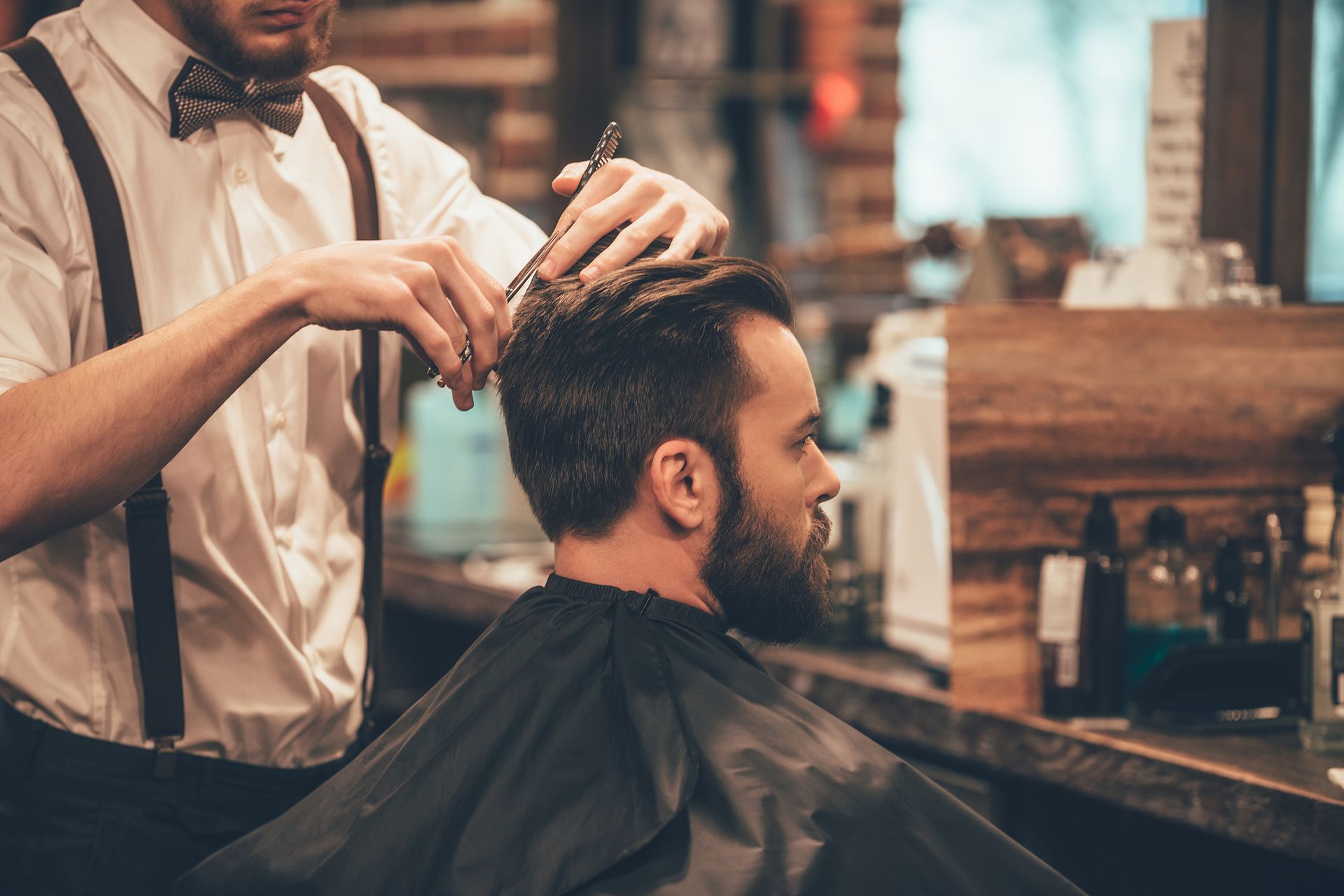 A man is getting his haircut by a barber in a barber shop.