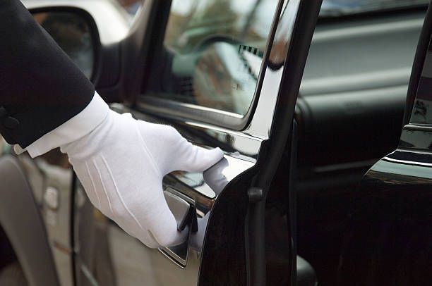 A suited individual with a white glove opens the door of a black car, symbolizing luxury limo rental service.