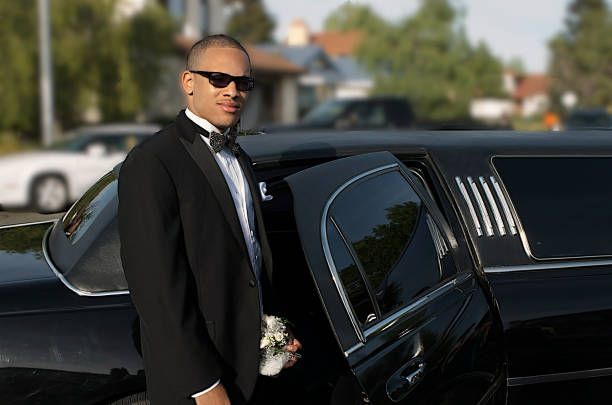 A man in a tuxedo stands beside a black limousine, showcasing a luxury limo rental service.