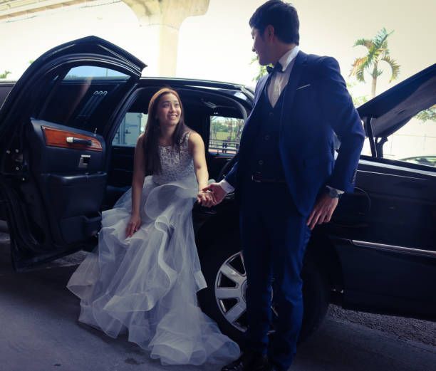 A bride in a white gown and groom in a suit getting into a wedding limo, marking the start of their new life together.