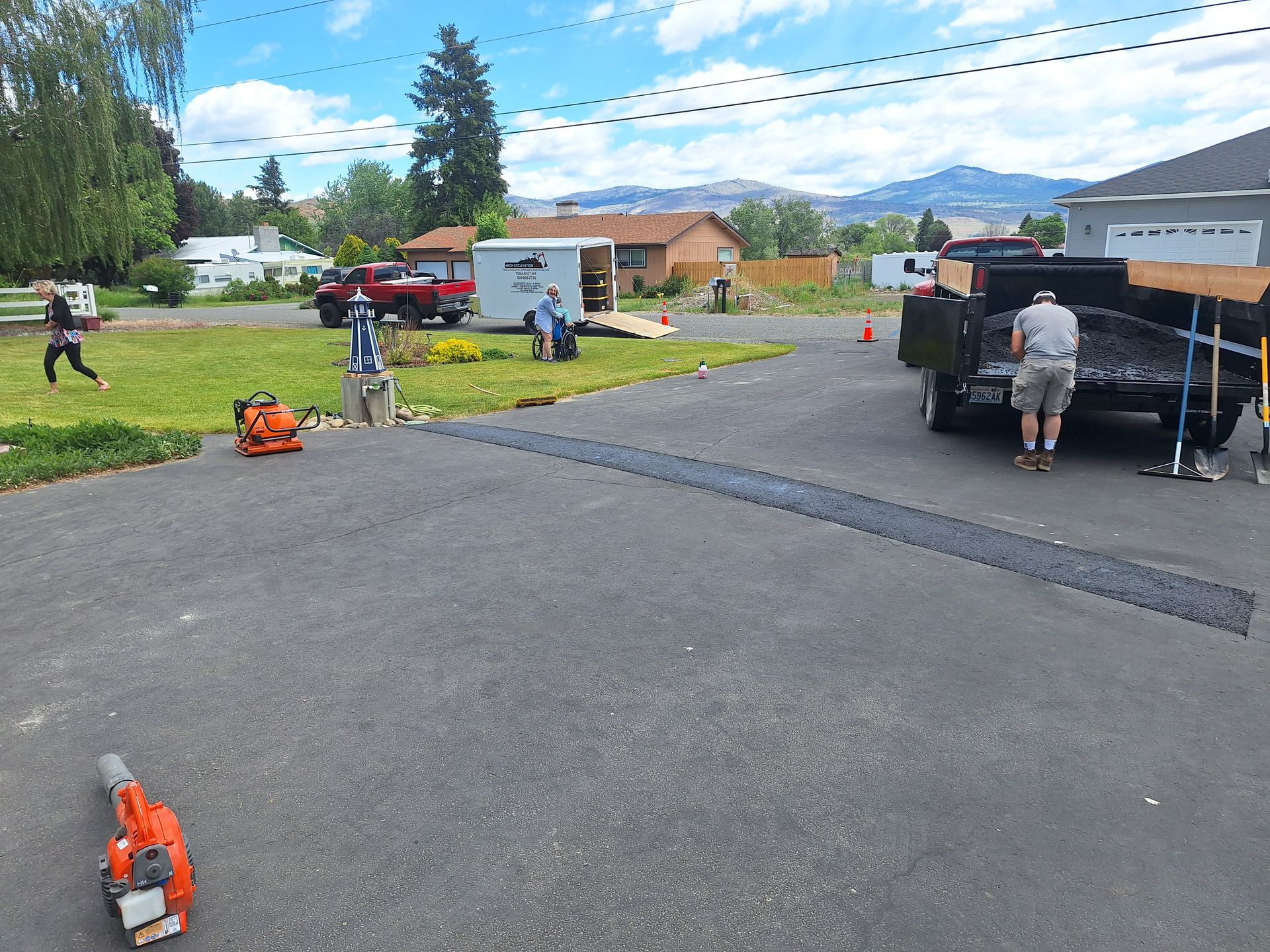 Workers landscaping a residential yard. Black truck, lawn blower, tools, grass, and houses.