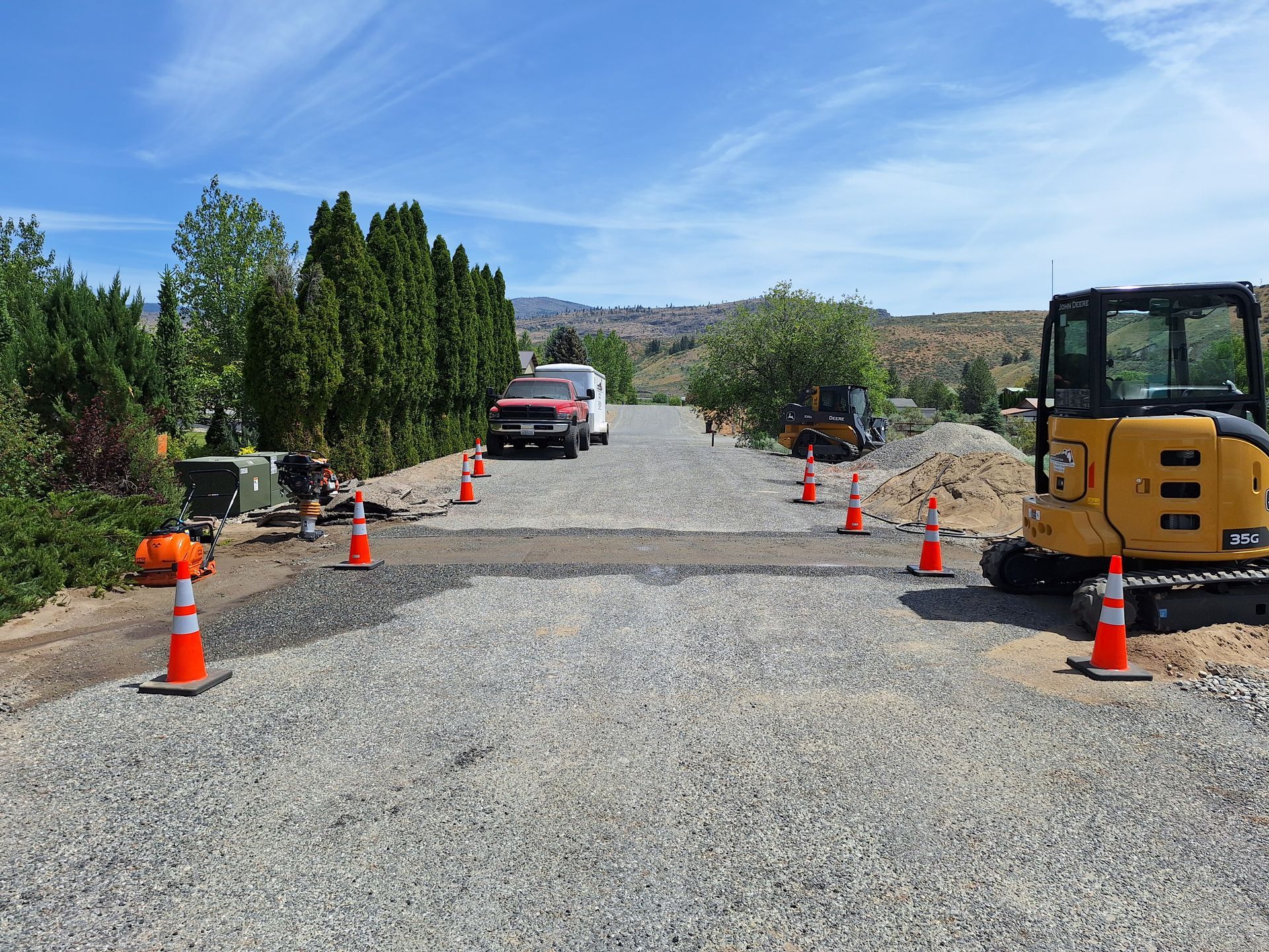 Construction scene: driveway being paved, surrounded by cones and equipment on a sunny day.