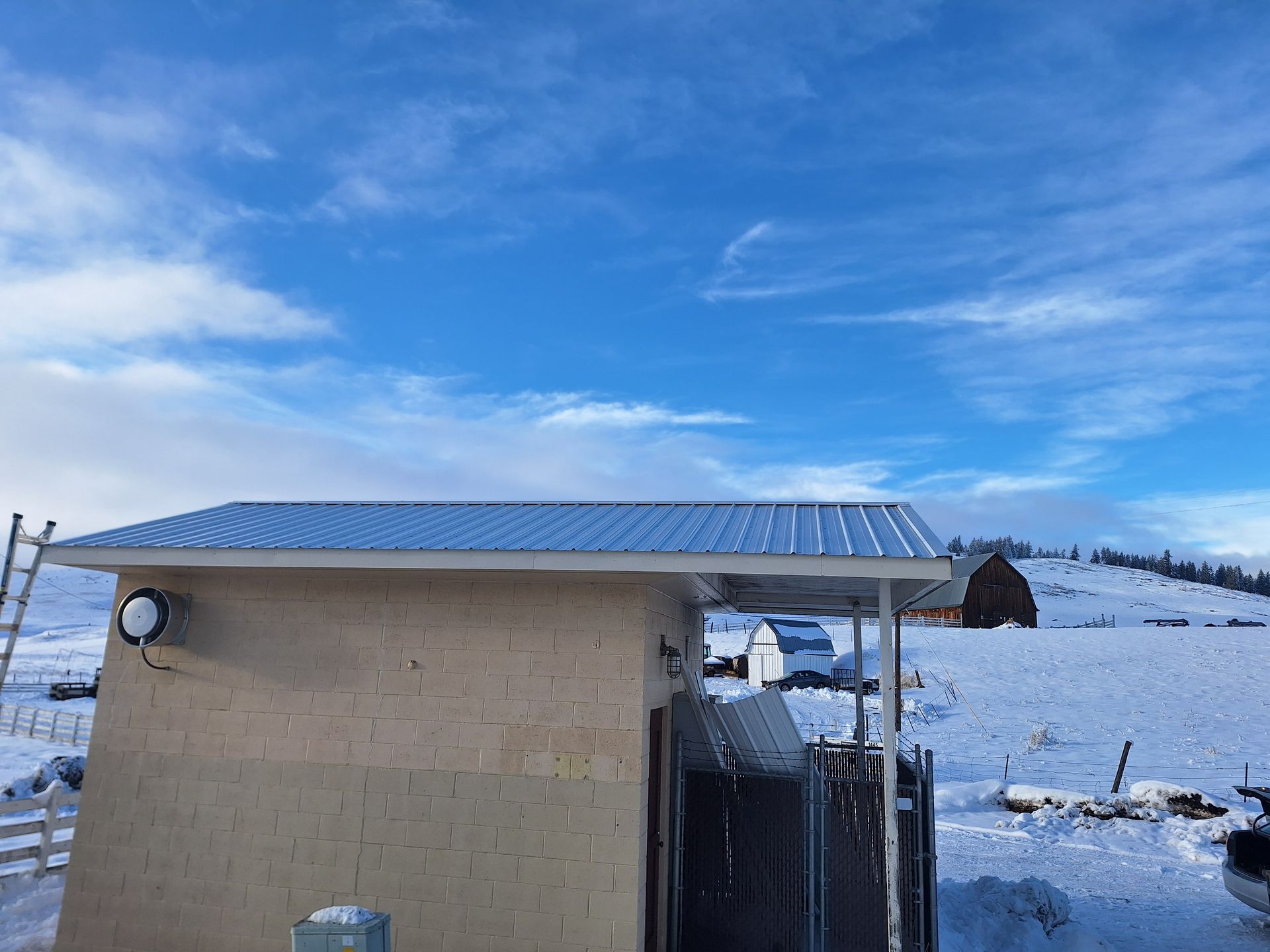 Building with a silver roof, snow-covered landscape, blue sky with clouds.