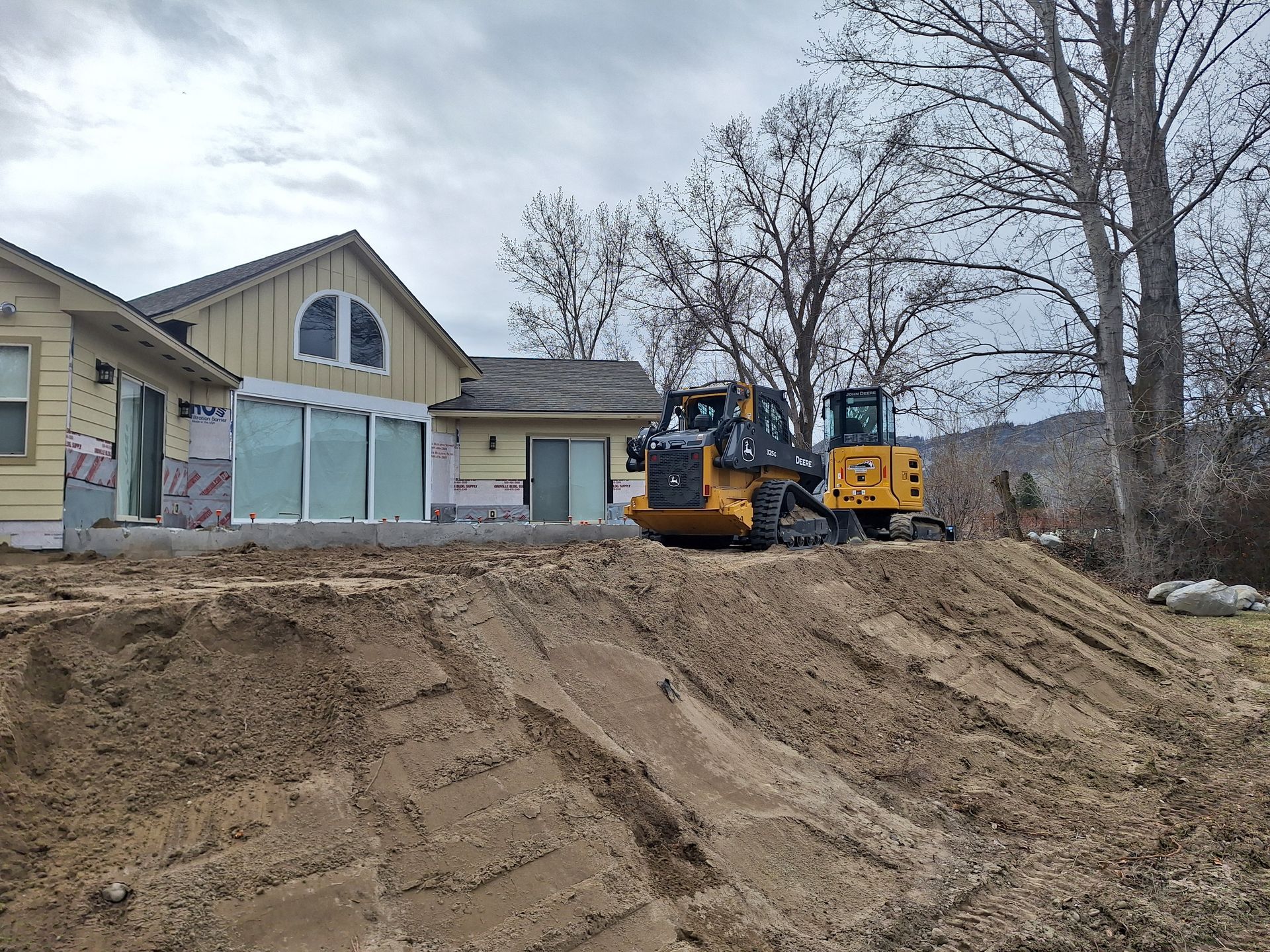 Yellow bulldozer on dirt pile near a house under construction.
