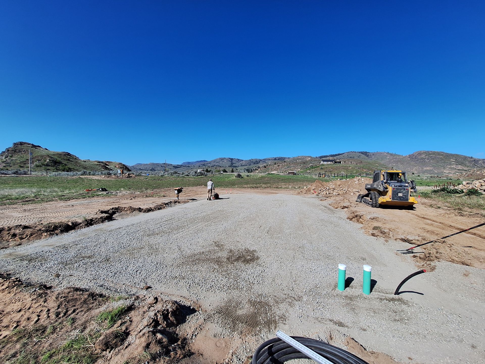 Construction site with gravel base, yellow loader, workers, and blue sky.