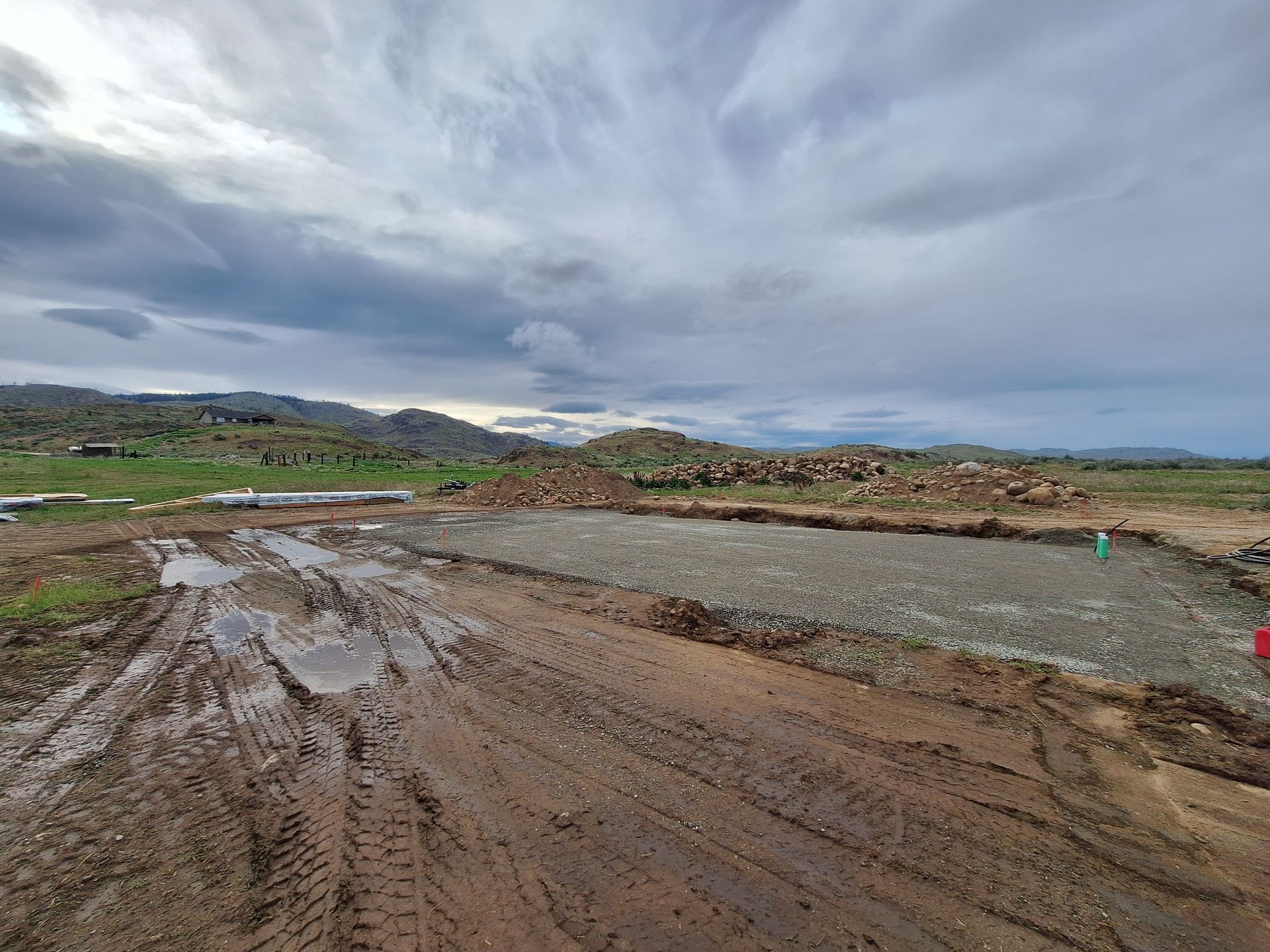 Muddy construction site with gravel base, cloudy sky, distant hills.