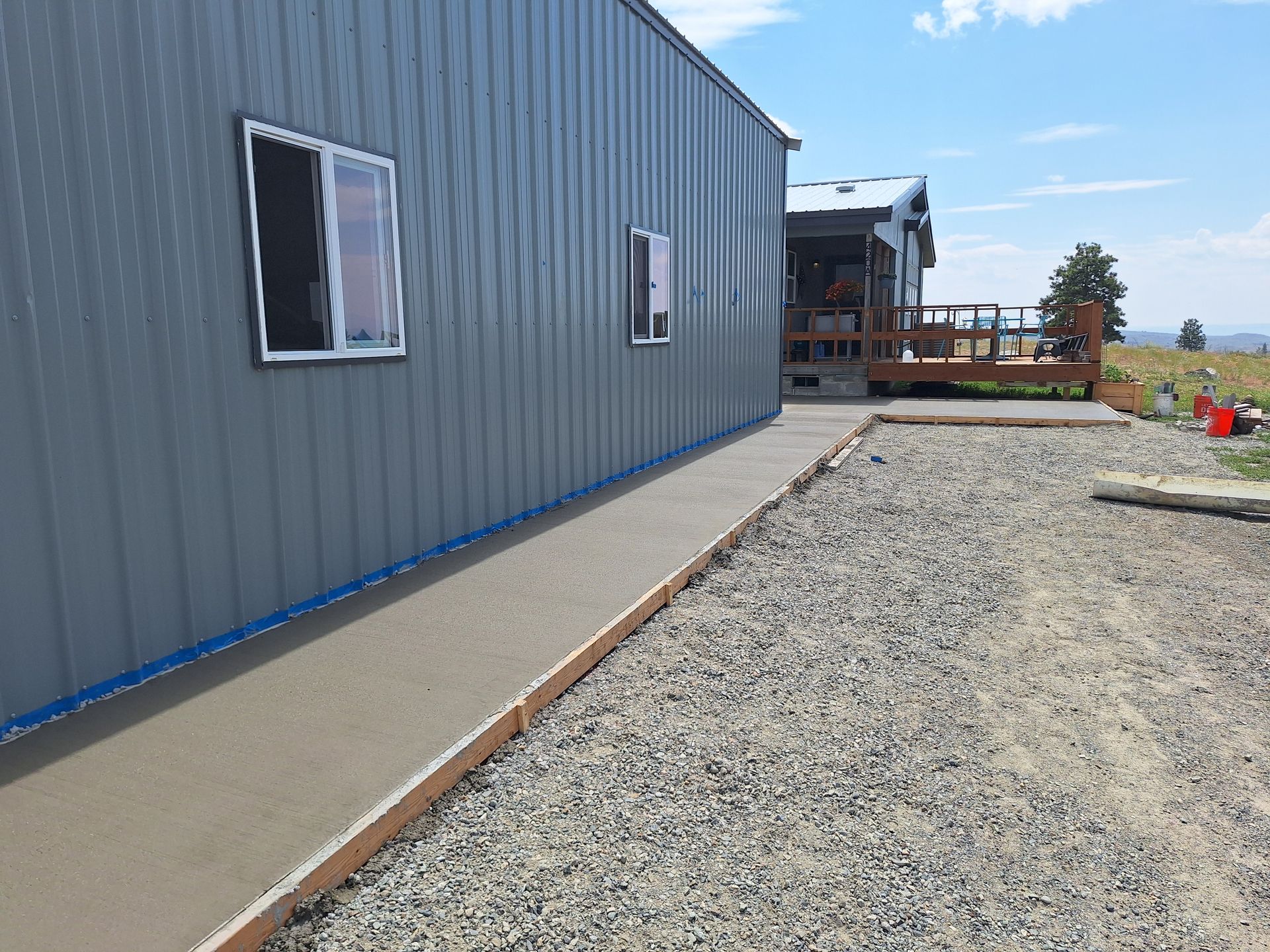 Concrete sidewalk alongside a gray building with windows, bordered by gravel and wooden timbers.