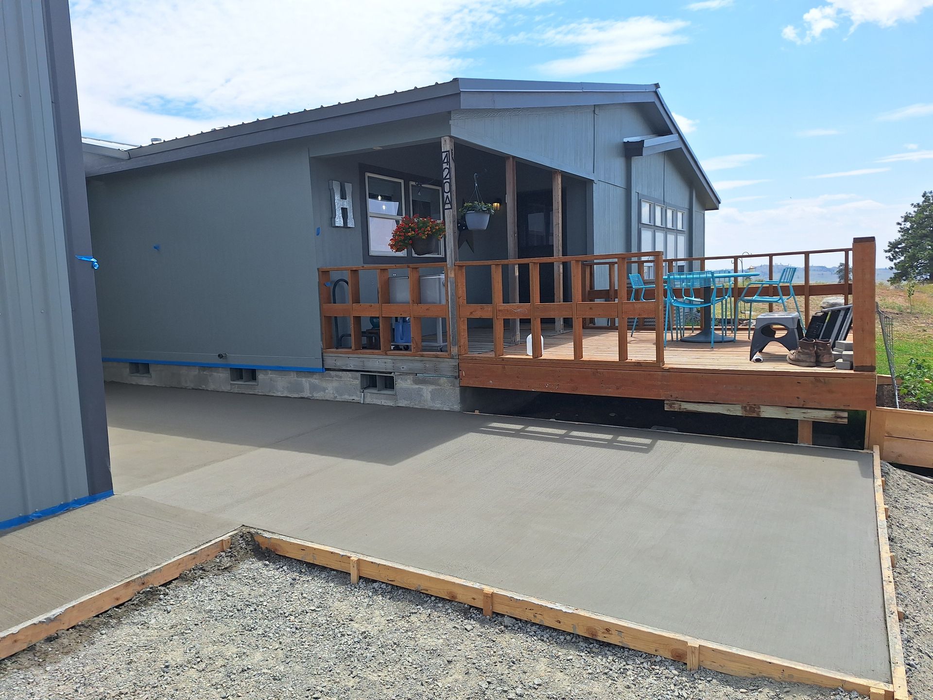 A house with a concrete patio and wooden deck, set against a sunny sky.