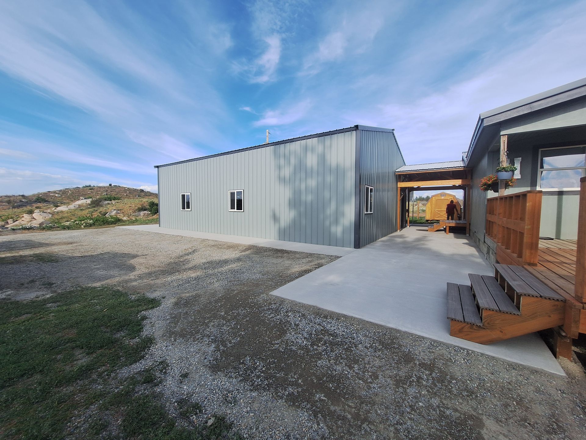 Gray metal building and wood deck connected by a concrete patio under a blue sky.
