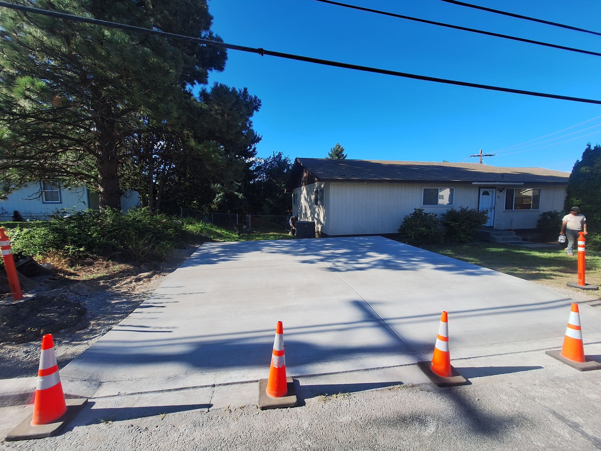 Newly paved concrete driveway with orange safety cones, in front of a house.
