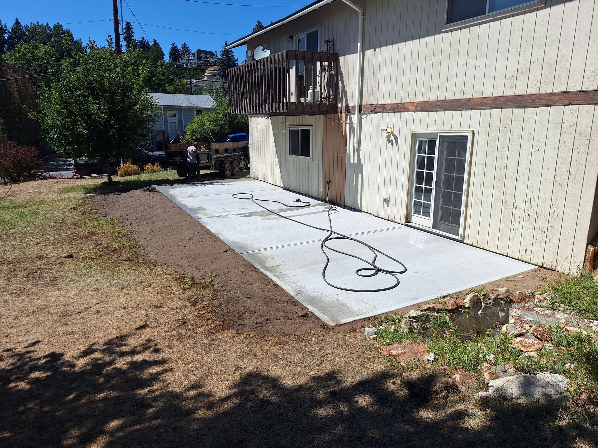 Newly poured concrete patio next to a two-story house, with a hose coiled on its surface.