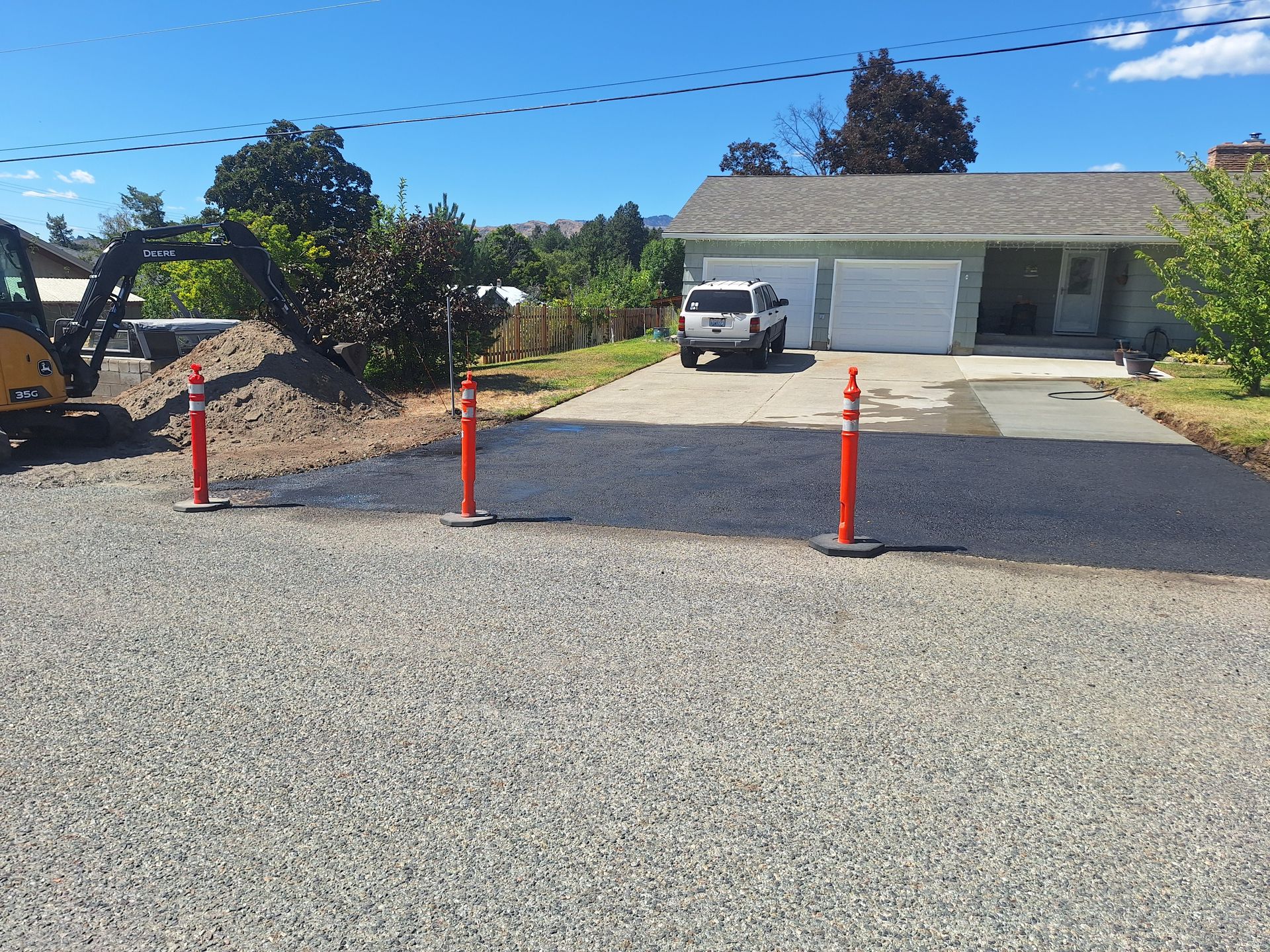Driveway with fresh asphalt. Orange poles separate gravel from the new surface.  A truck sits on the drive.