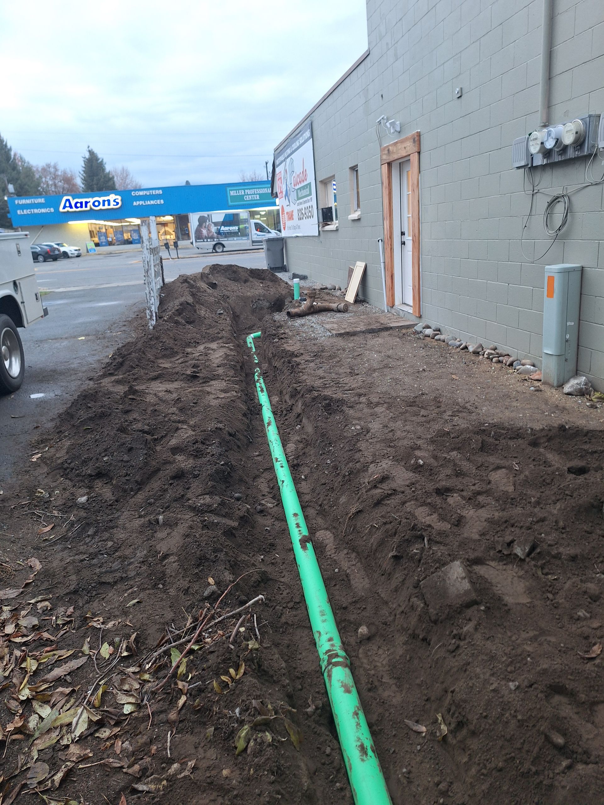 Green pipe in a trench along a building. Construction site.