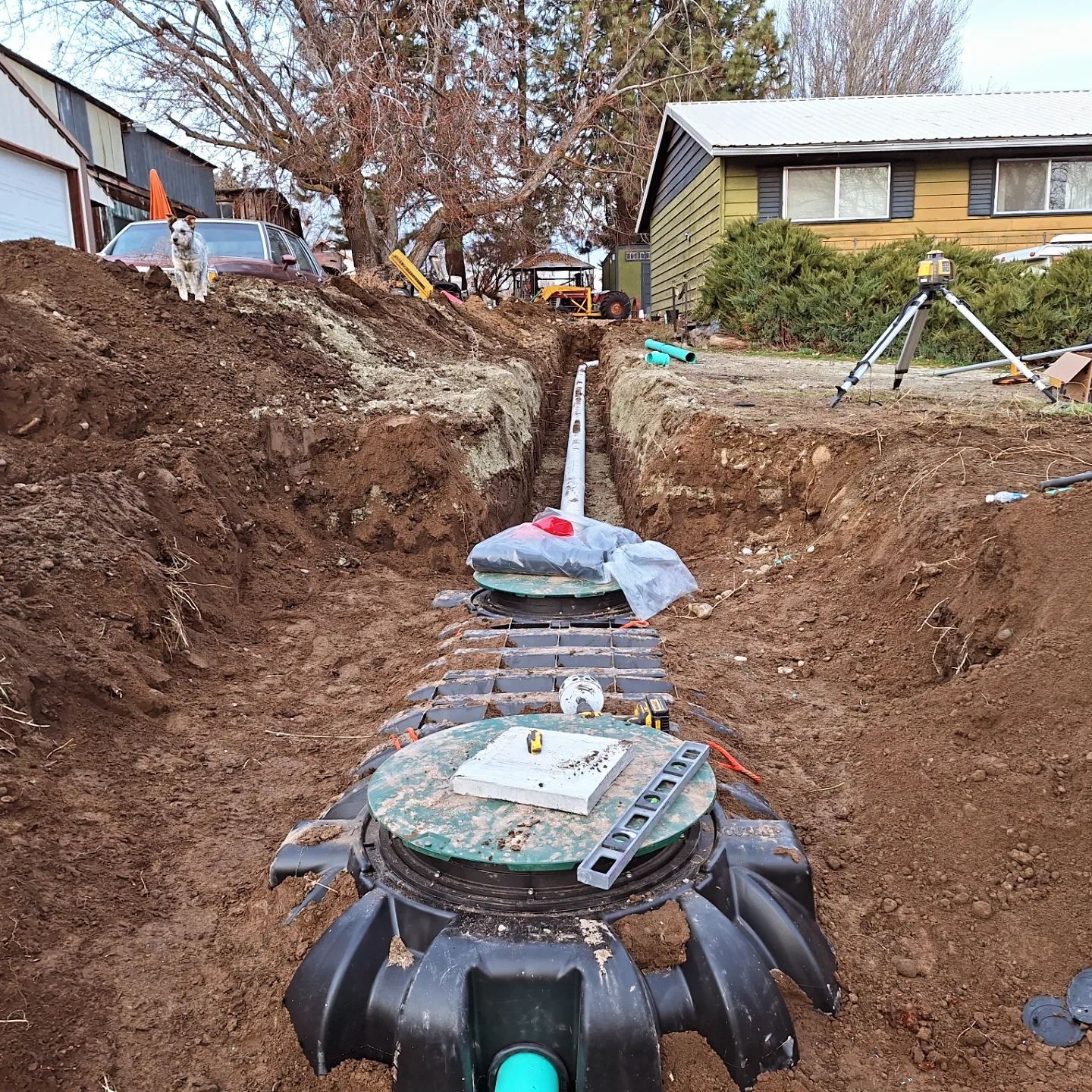 Construction site with an open trench, septic tank, and tools.