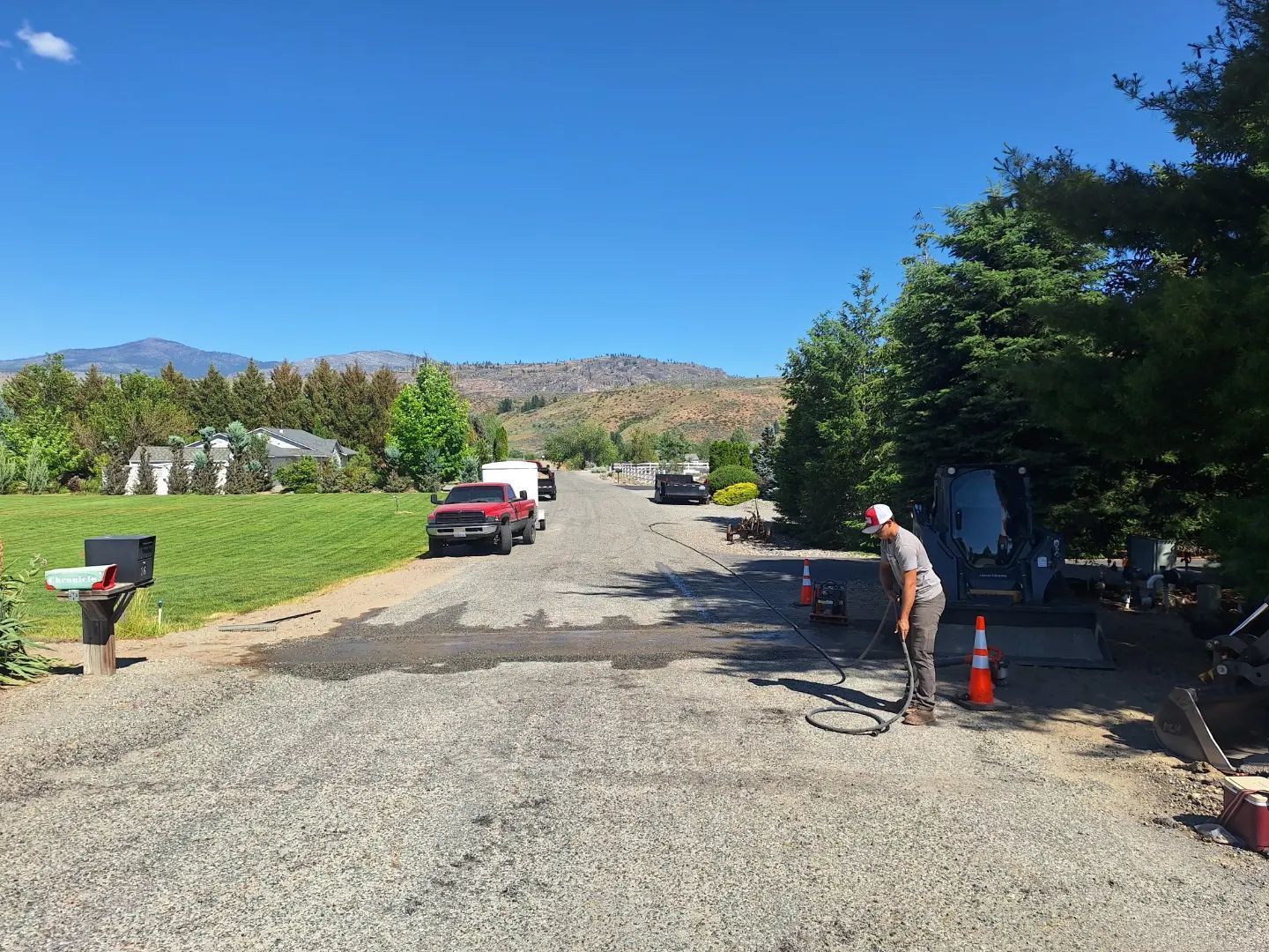 Gravel road with a person working, red truck, and distant mountains under a blue sky.
