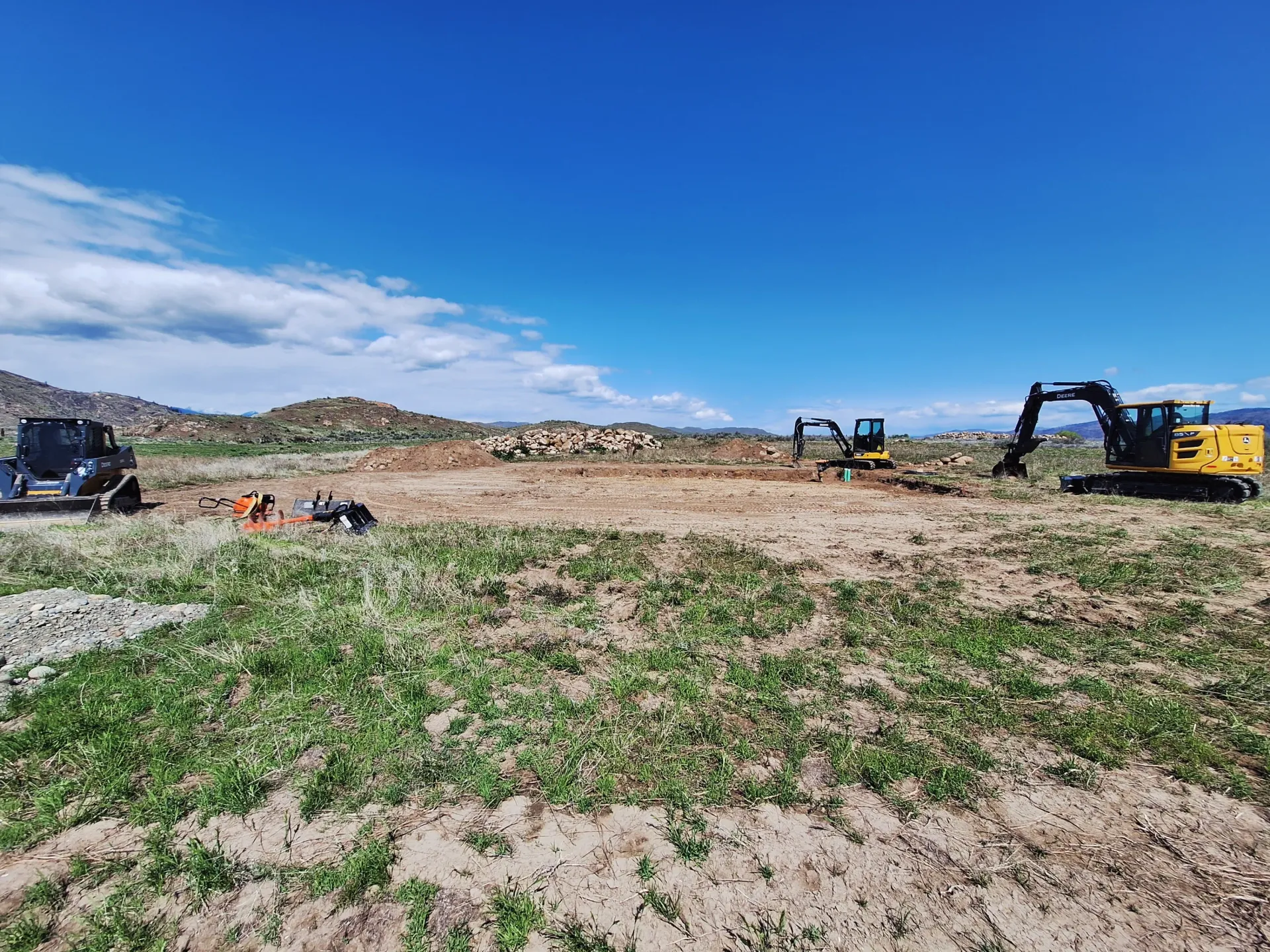 Construction site with excavators and cleared land under a blue sky.