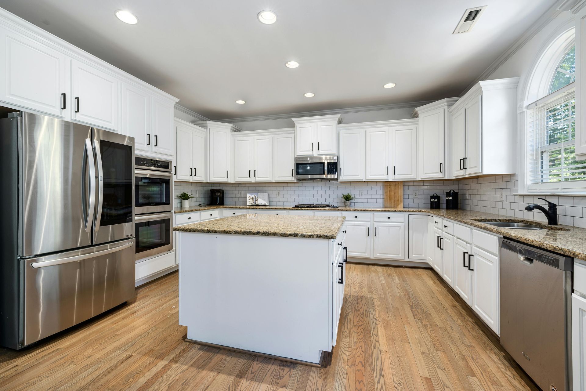 White kitchen with stainless steel appliances, granite countertops, and light wood flooring.