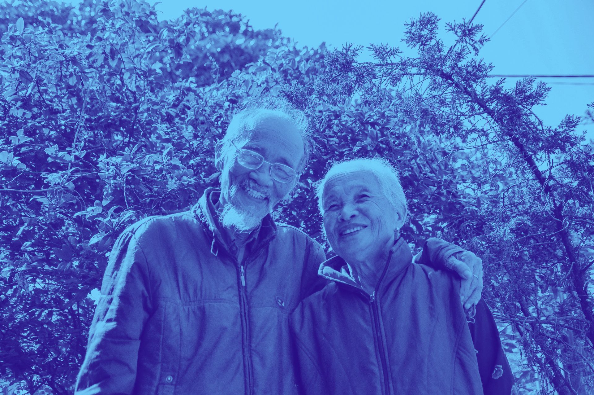 A man and a woman are posing for a picture in front of trees.