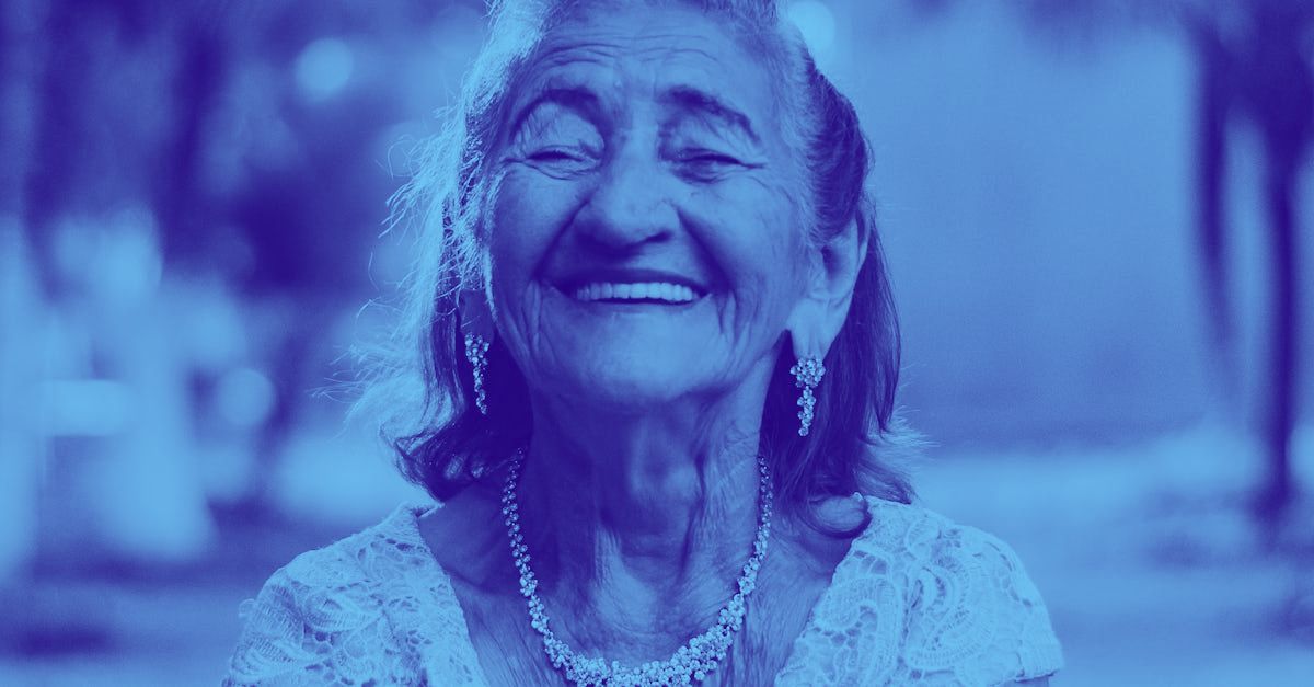 An elderly woman is smiling in a blue and white photo.