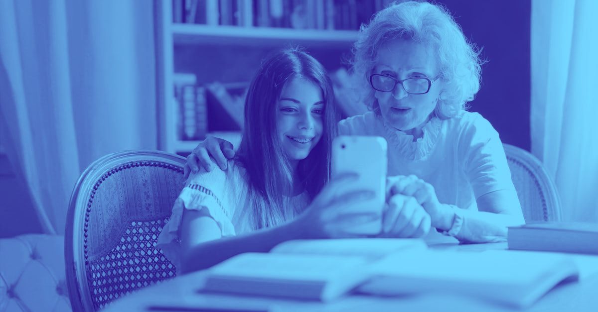 An elderly woman and a young girl are sitting at a table looking at a cell phone.